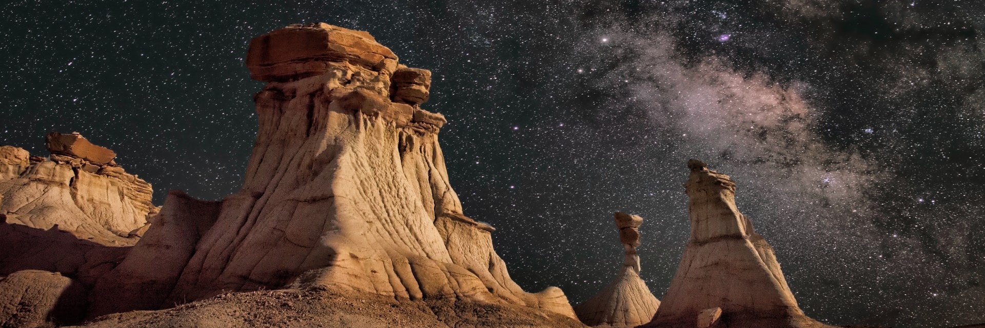A rock formation in a warm artificial, behind the beautiful, purple-blue night sky with many stars